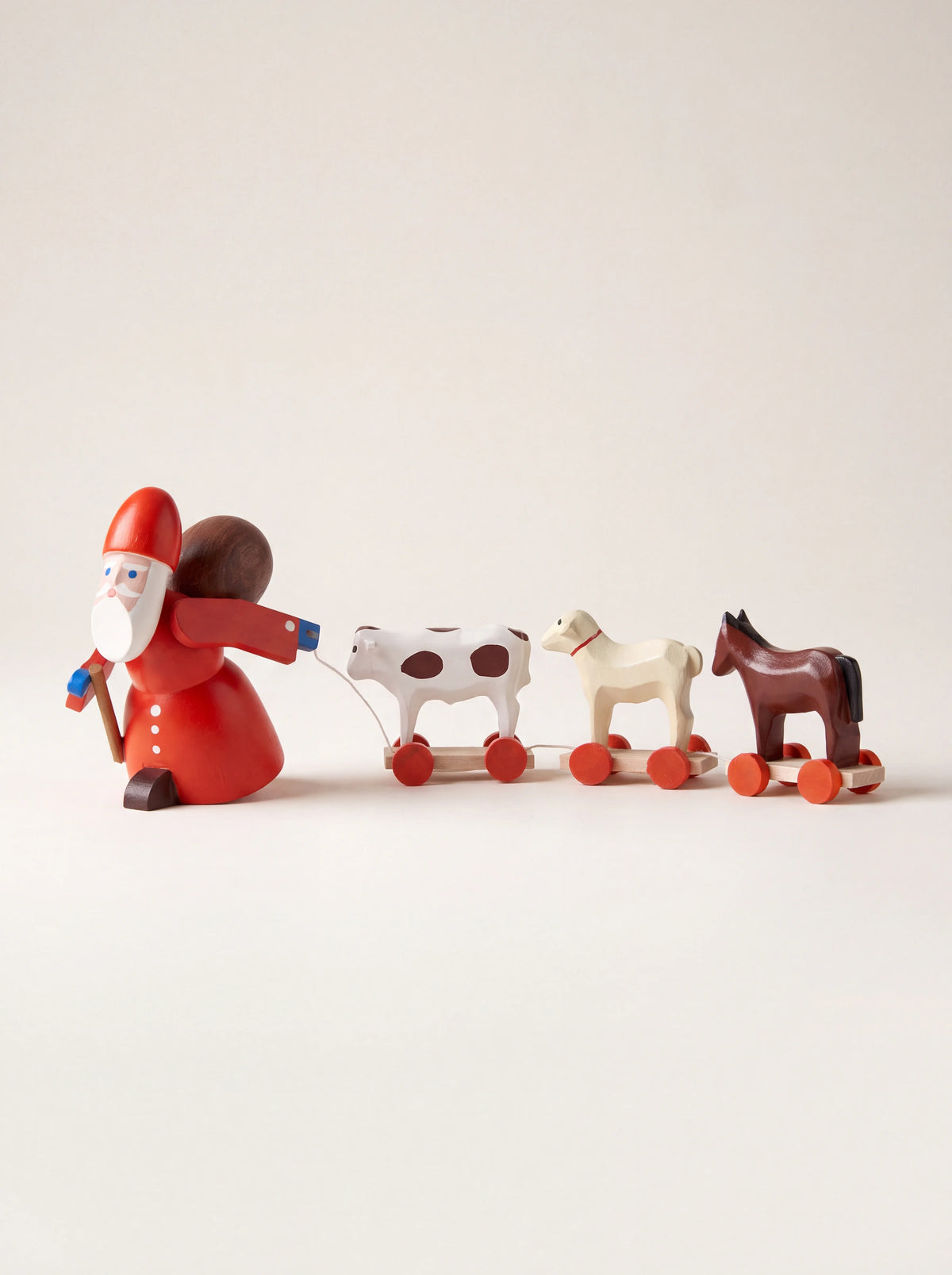Painted wooden Santa Claus figurine in red pulling three wheeled toy animals on a cord