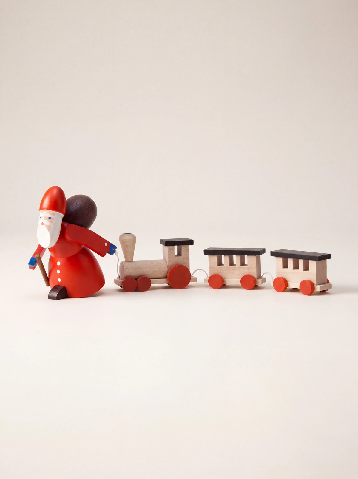 Painted wooden Santa figurine in a red coat pulling a miniature wooden train with two carriages
