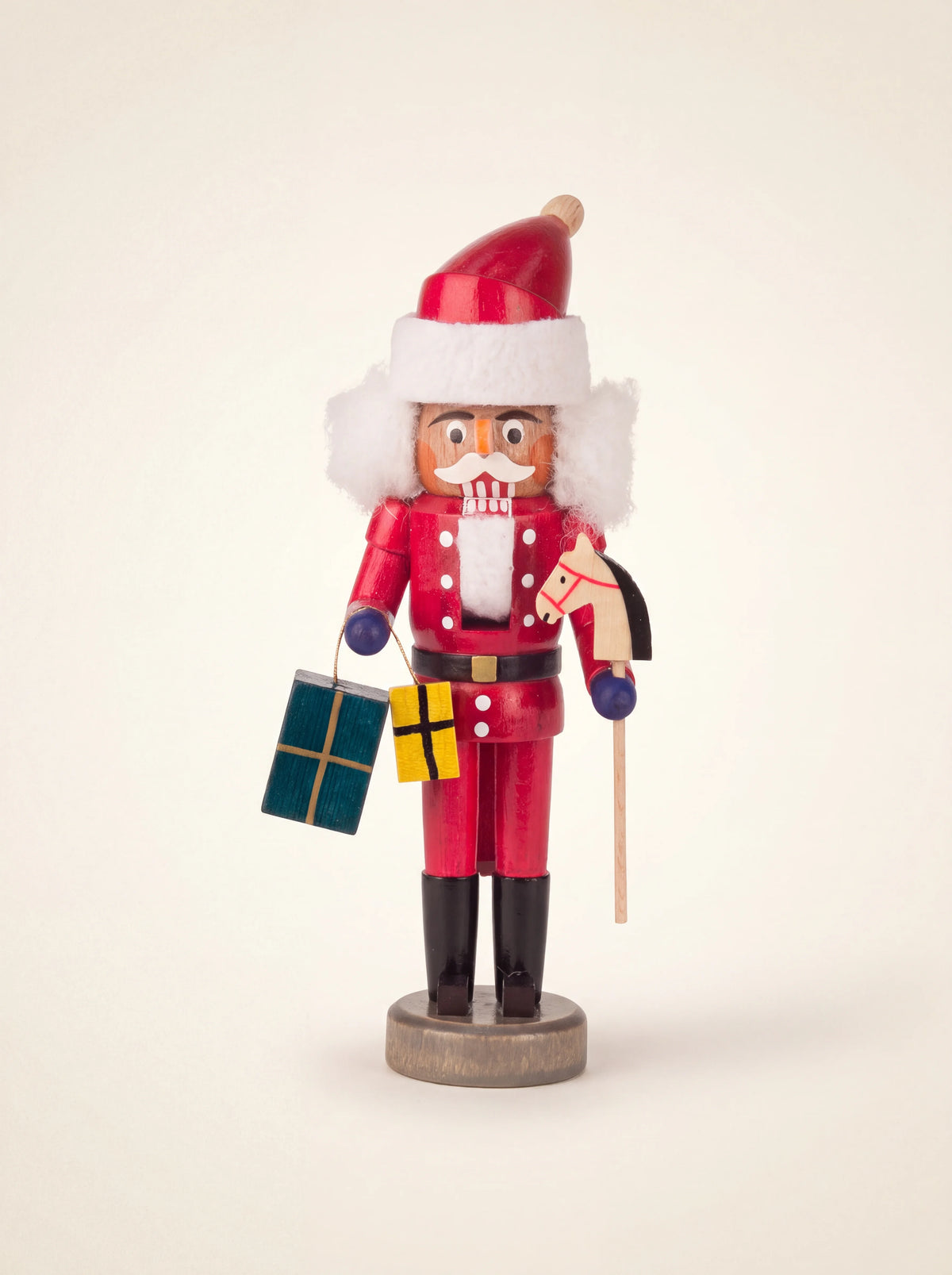 Red wooden Santa nutcracker holding two small presents and a hobby horse, standing on a round base