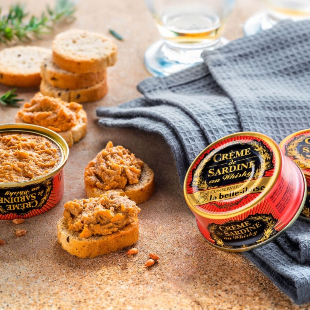 Open tin of sardine cream alongside toasted baguette slices topped with the spread