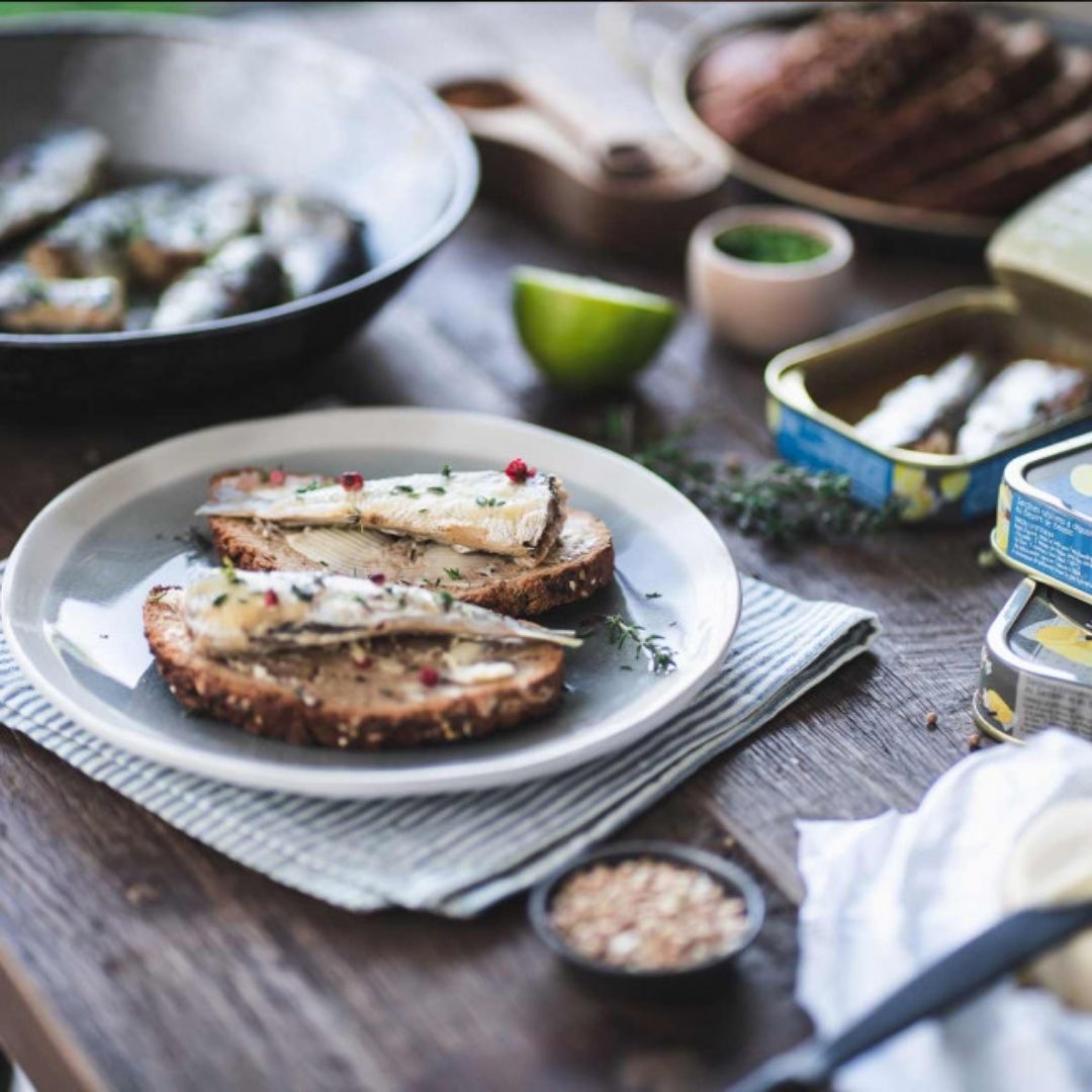 Two sardines served warm on sliced bread with herbs and pink peppercorns on a ceramic plate