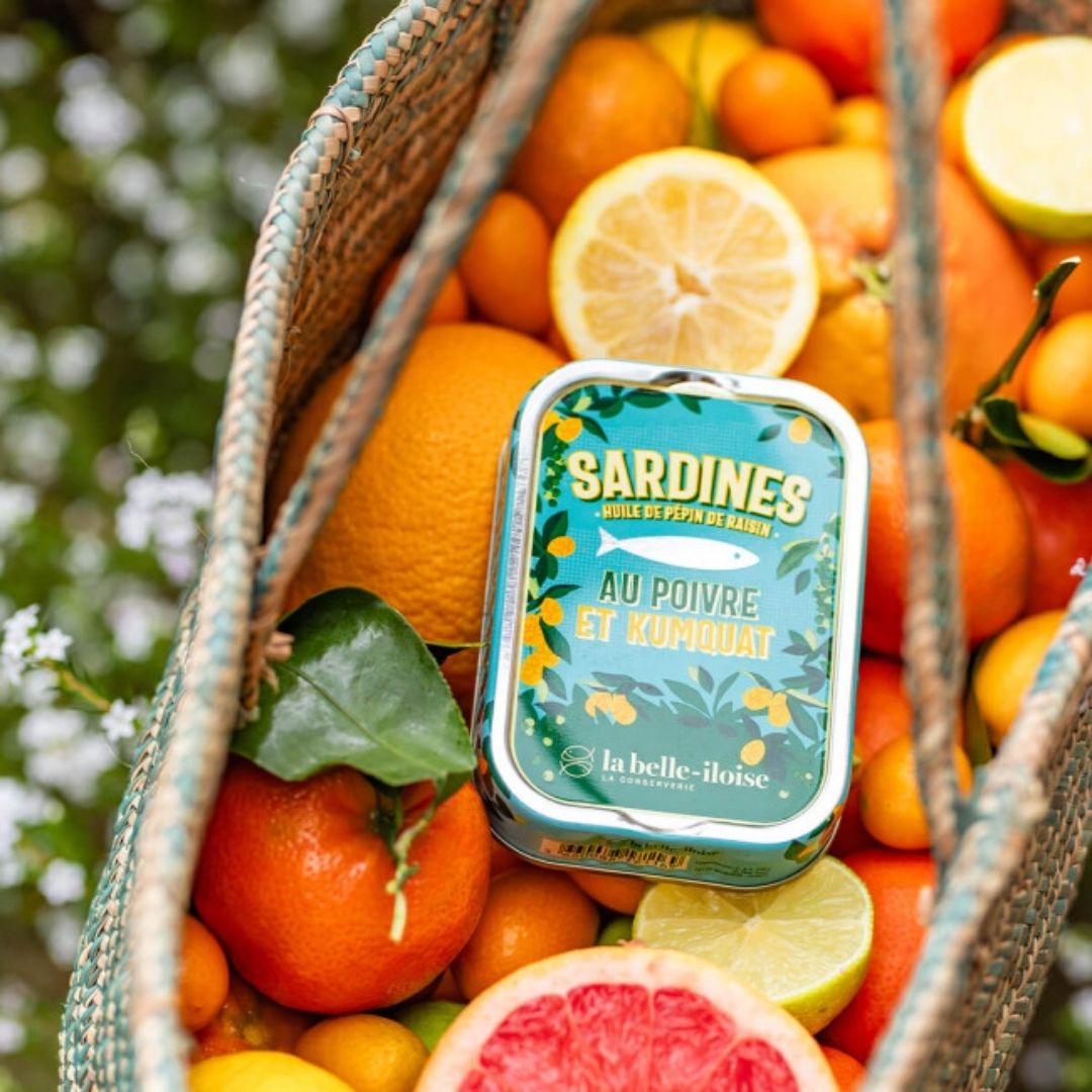 Tin of sardines resting inside a woven basket filled with assorted whole and sliced citrus fruit