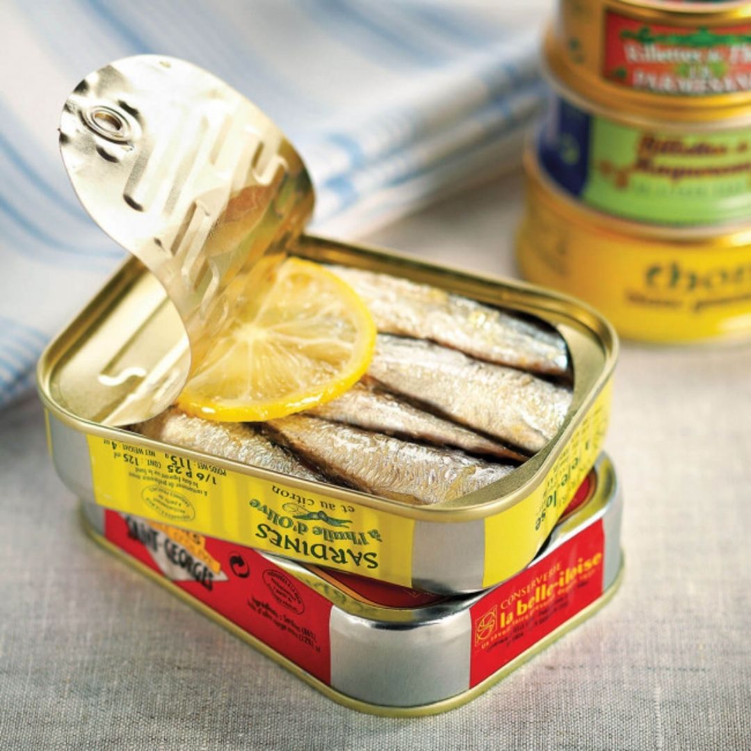 Opened tin revealing whole sardines packed in olive oil and garnished with a lemon slice