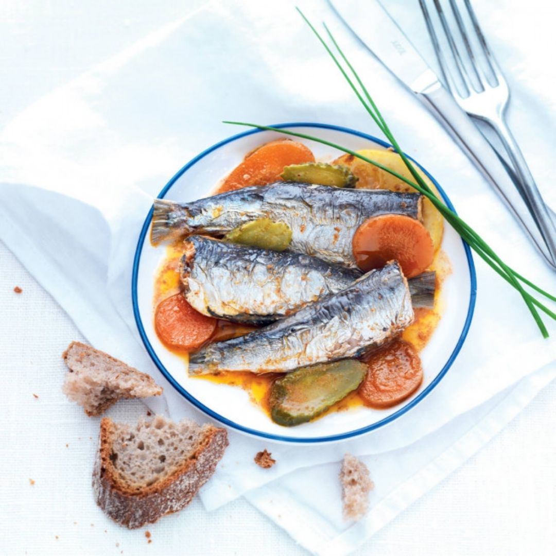 Sardines served on a plate with sliced carrots, gherkins, sauce, chives and crusty bread