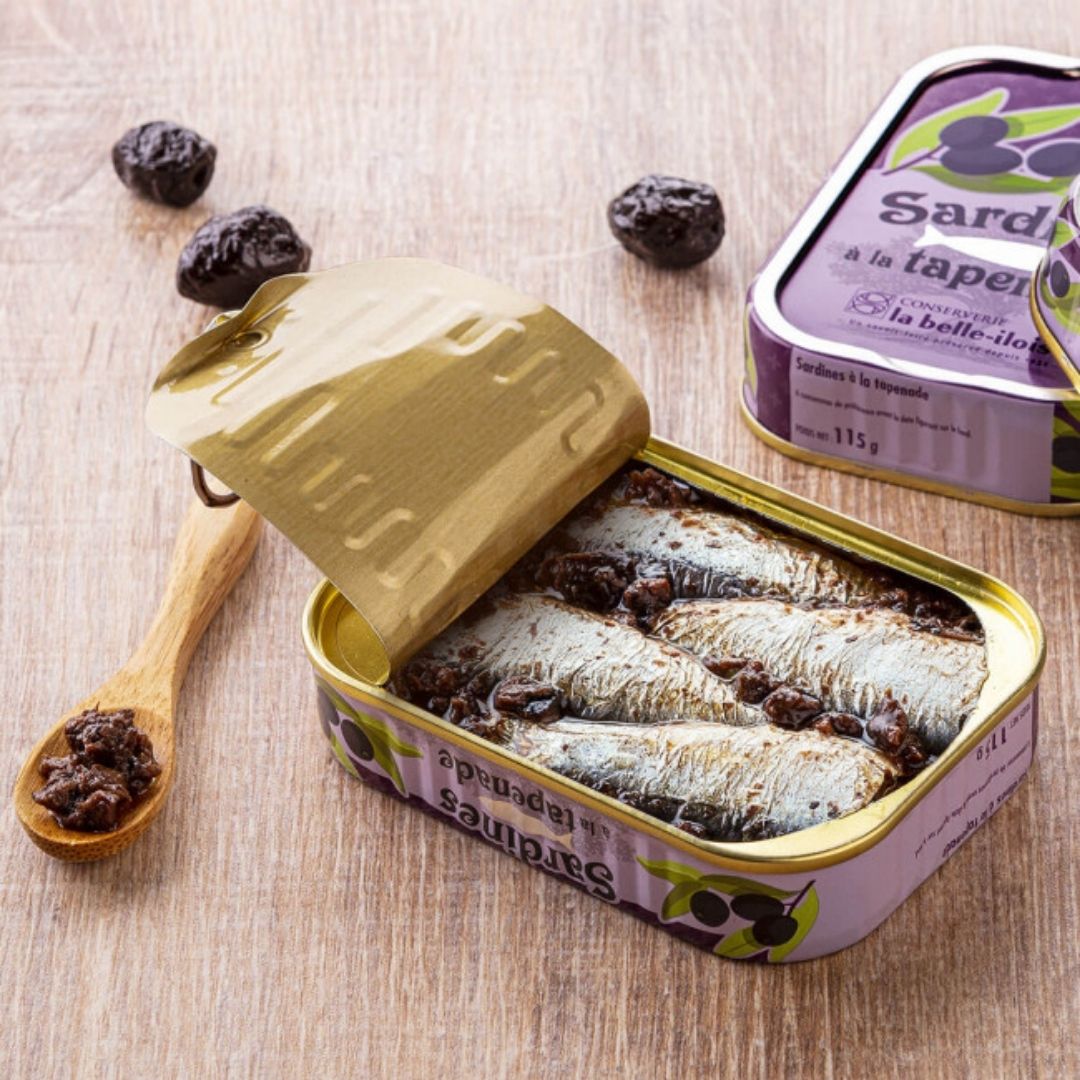 Opened tin showing whole sardines packed in olive tapenade sauce, with peeled-back lid