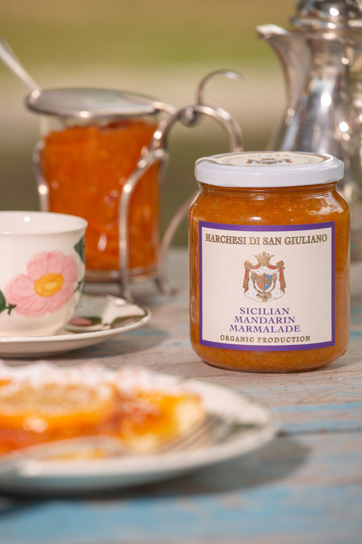 Sicilian mandarin marmalade jar on a table beside a slice of citrus tart and a floral teacup