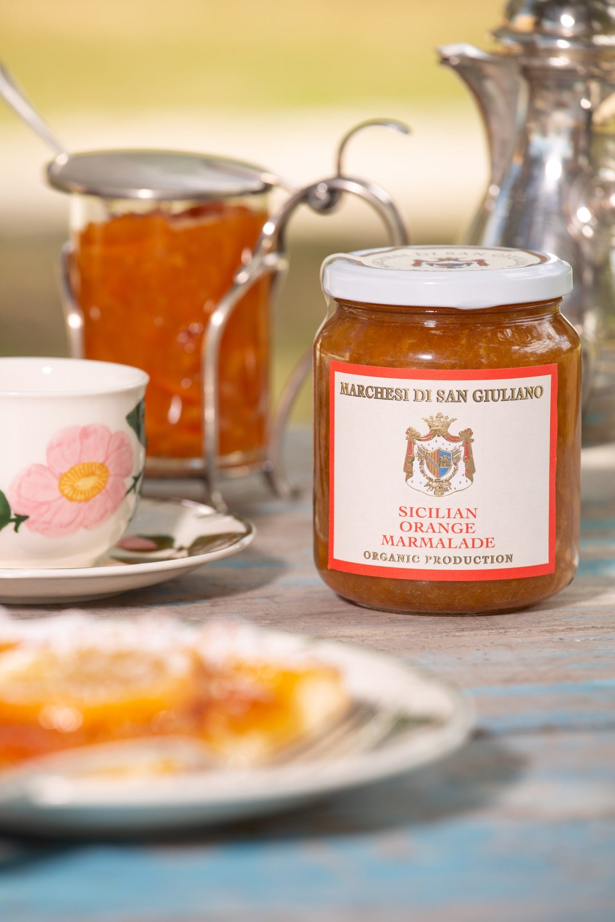 Sicilian orange marmalade jar on a table beside a floral teacup, a silver pot, and orange tart