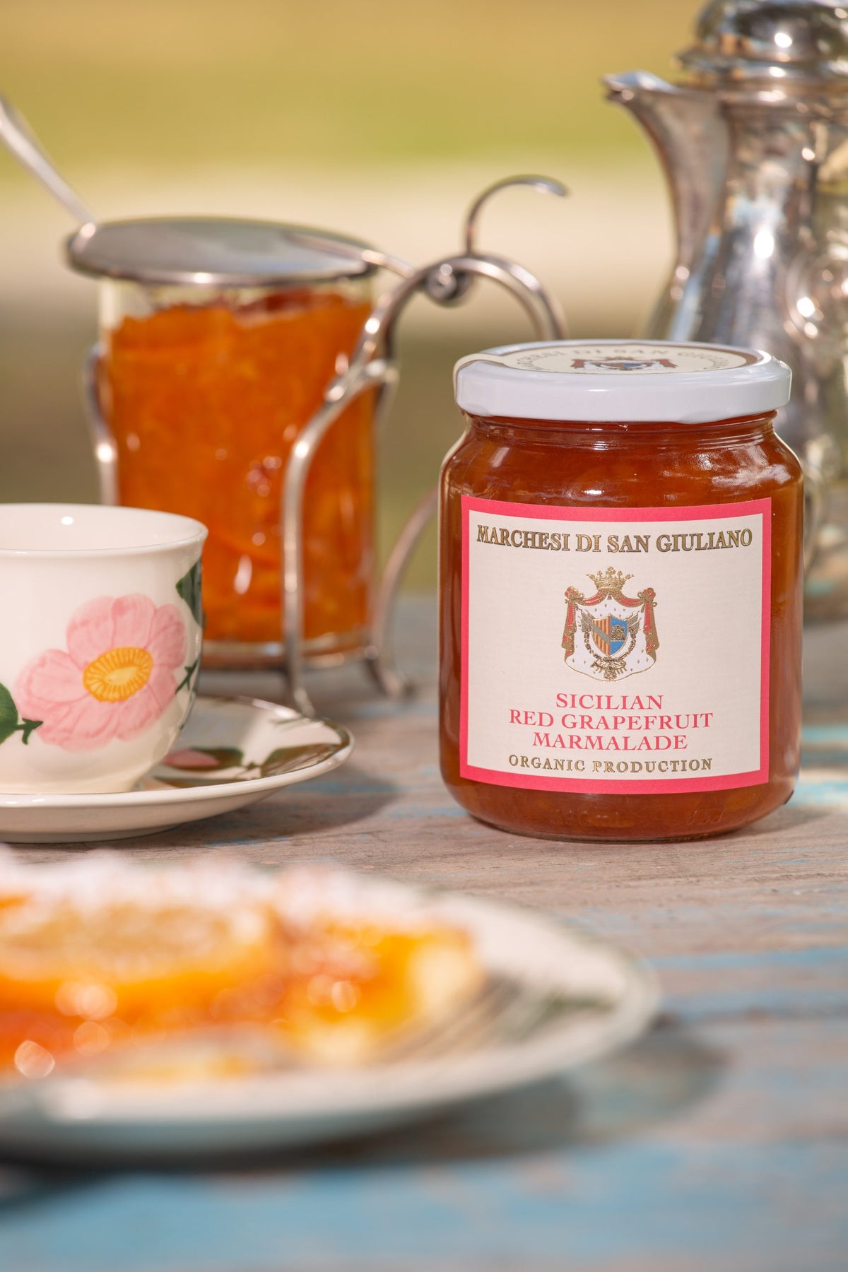 Jar of Sicilian red grapefruit marmalade on a breakfast table alongside a teacup and pastry