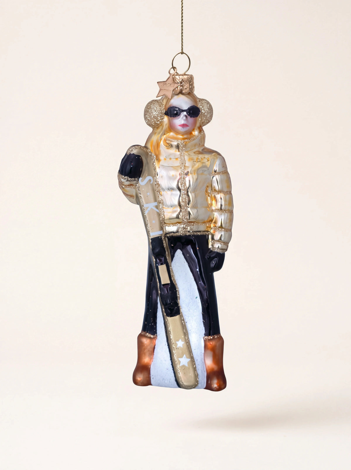 Glass skier ornament with a metallic gold puffer jacket, black trousers, sunglasses and ski