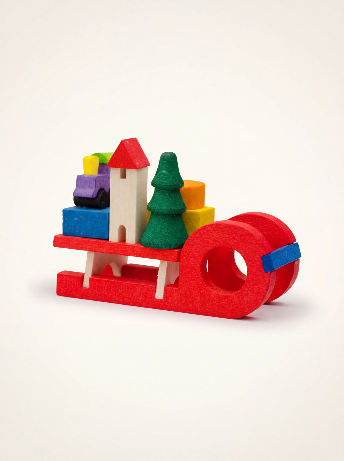 Red wooden sleigh ornament loaded with colourful miniature toys including a green tree, house, and train