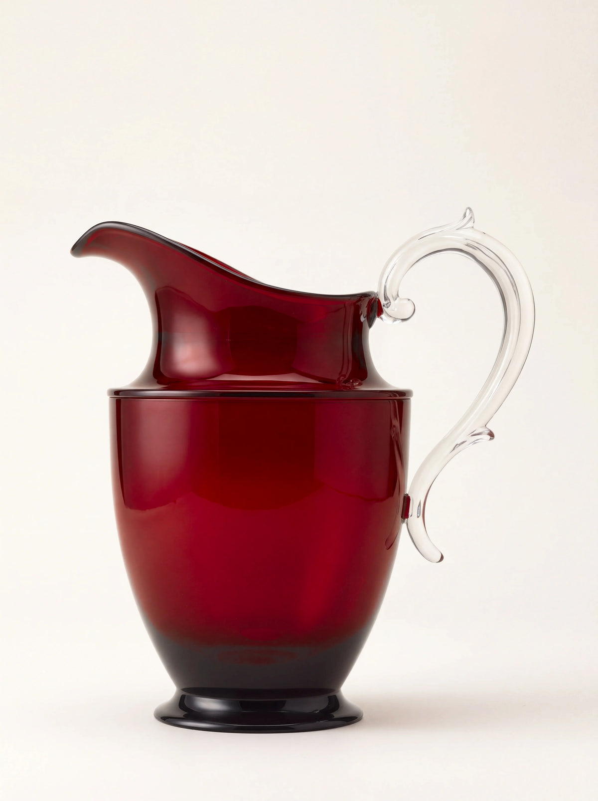 Ruby red acrylic pitcher with a curved spout, clear scrolled handle and circular footed base