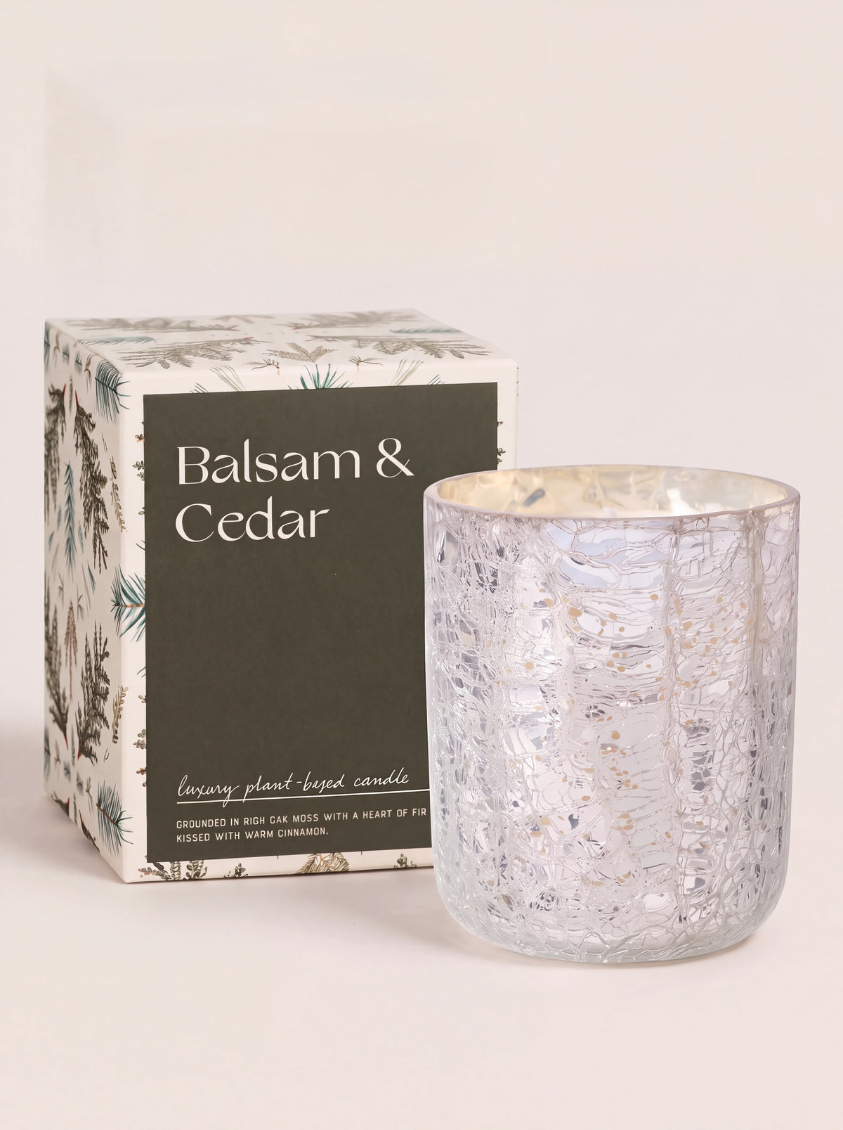 Scented candle in a silver crackle glass vessel beside its illustrated Balsam & Cedar packaging box