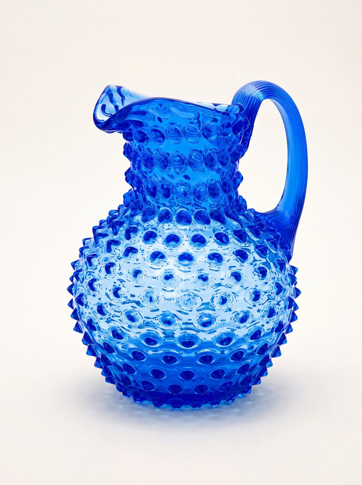 Blue hobnail glass jug with a rounded body, curved handle and pouring spout