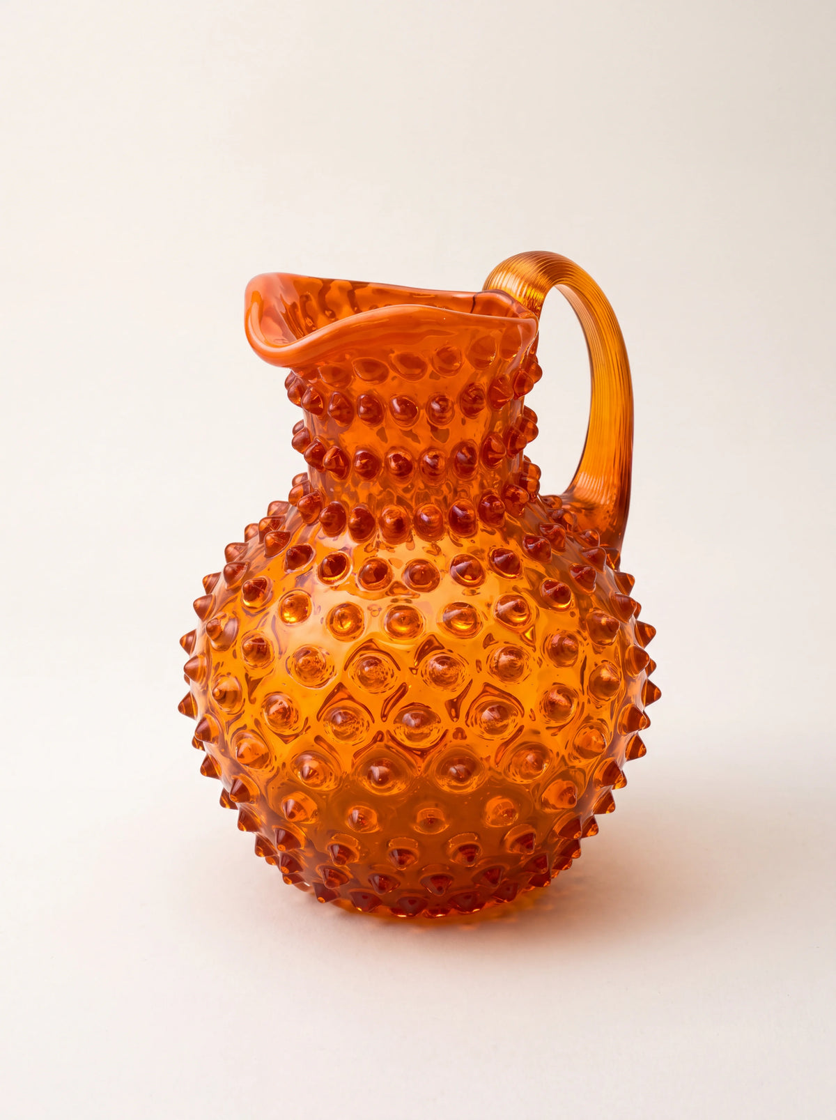 Orange hobnail glass jug with a bulbous body, flared pouring spout, and ribbed handle