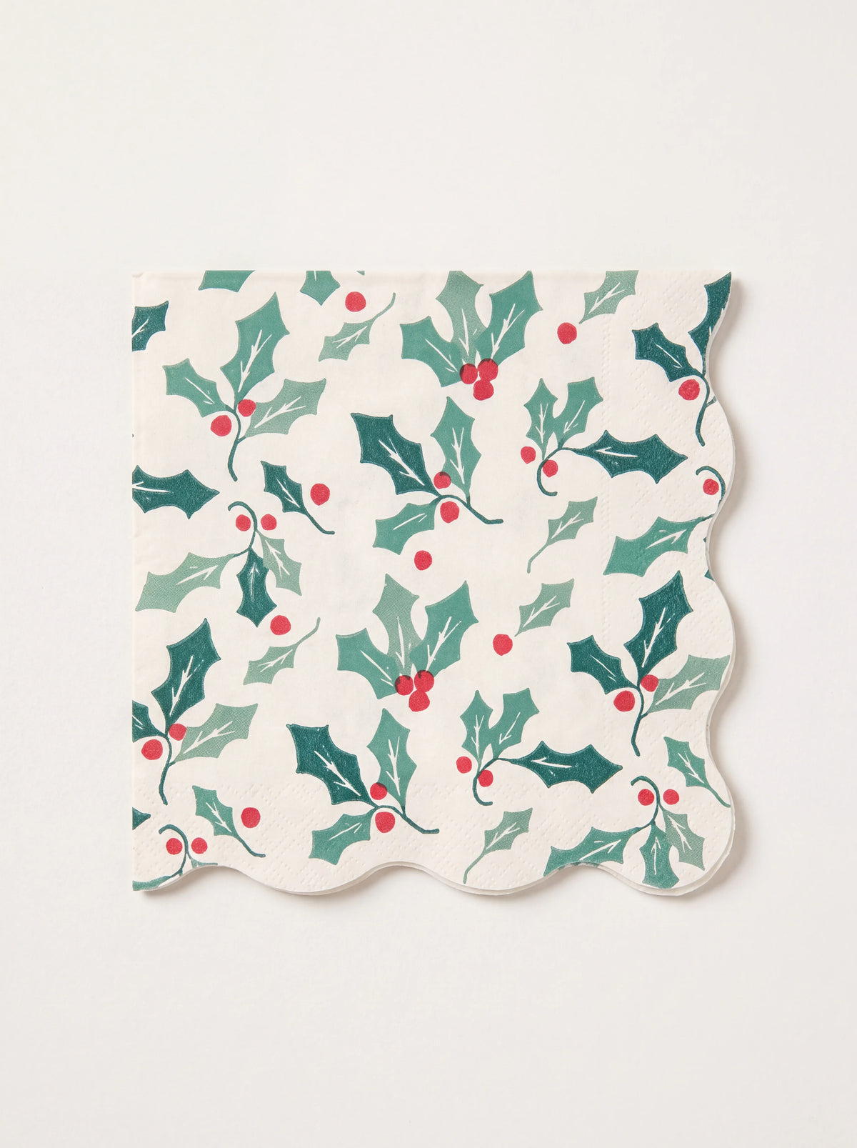 Small square paper napkin with scalloped edges and a printed green holly leaf and red berry pattern