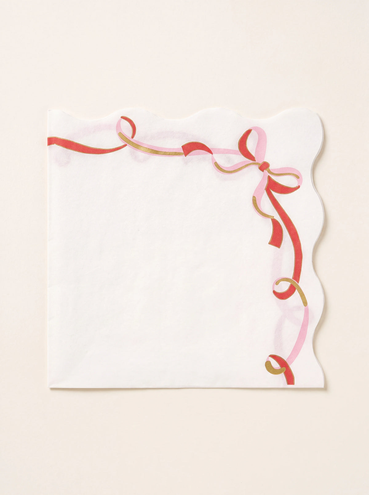 White paper napkin with scalloped edges and a printed pink and red ribbon bow with gold foil details