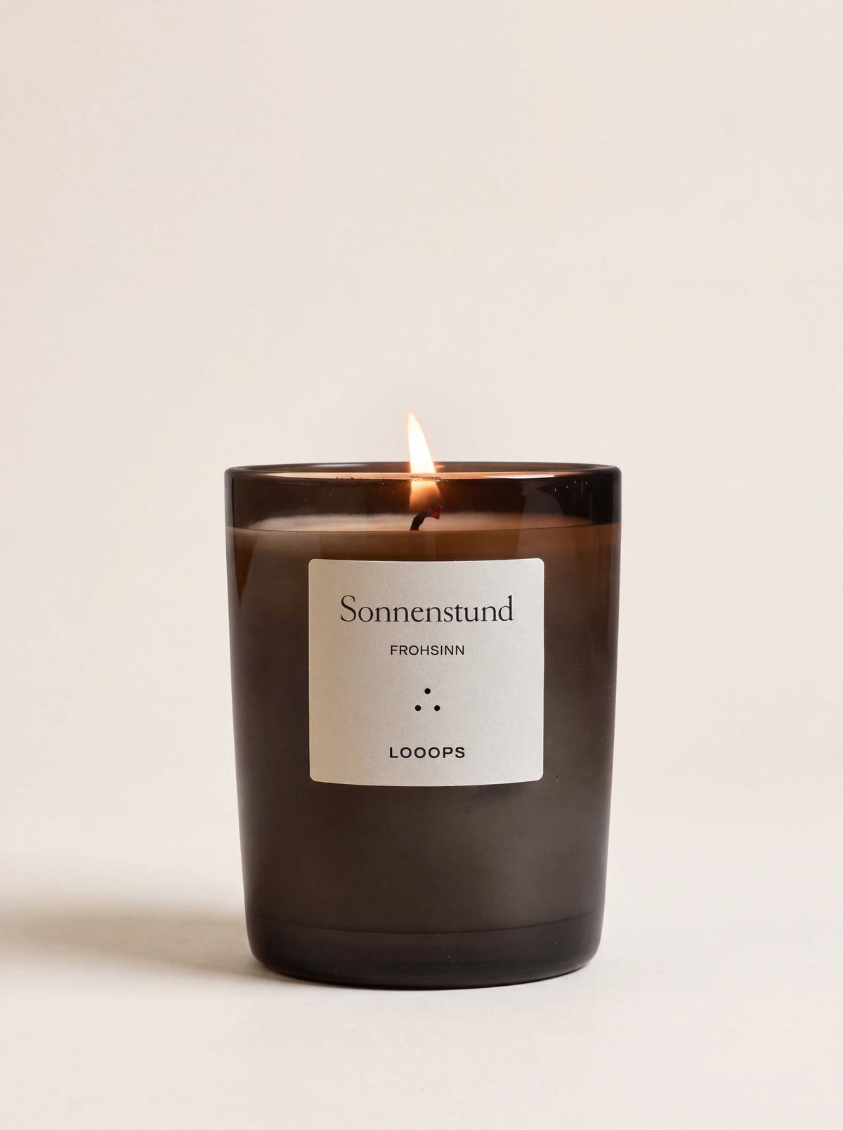 Lit scented candle in a dark glass jar with a label reading Sonnenstund FROHSINN LOOOPS