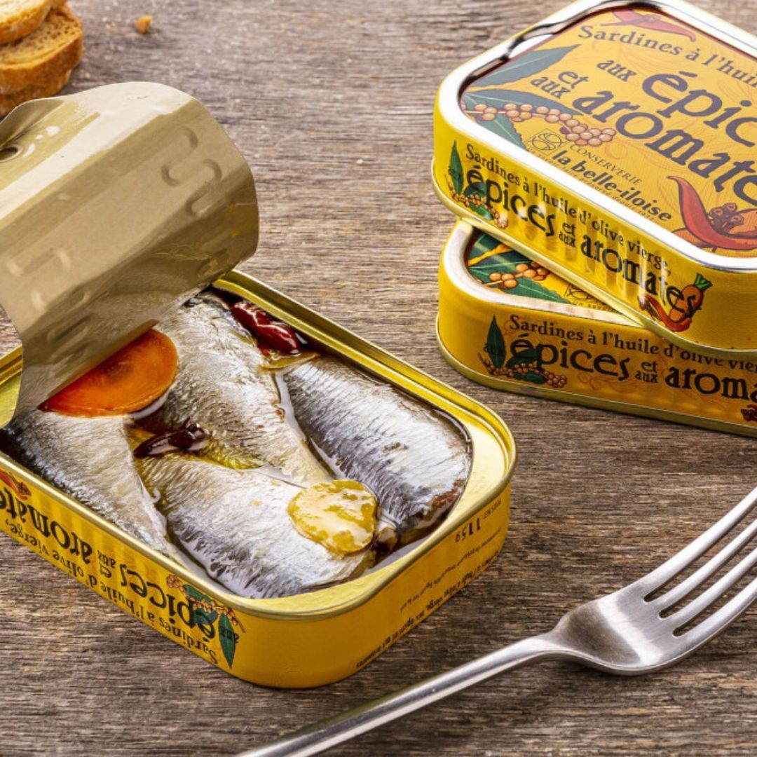 Opened tin of spiced sardines showing whole fish in olive oil with a carrot slice and chilli