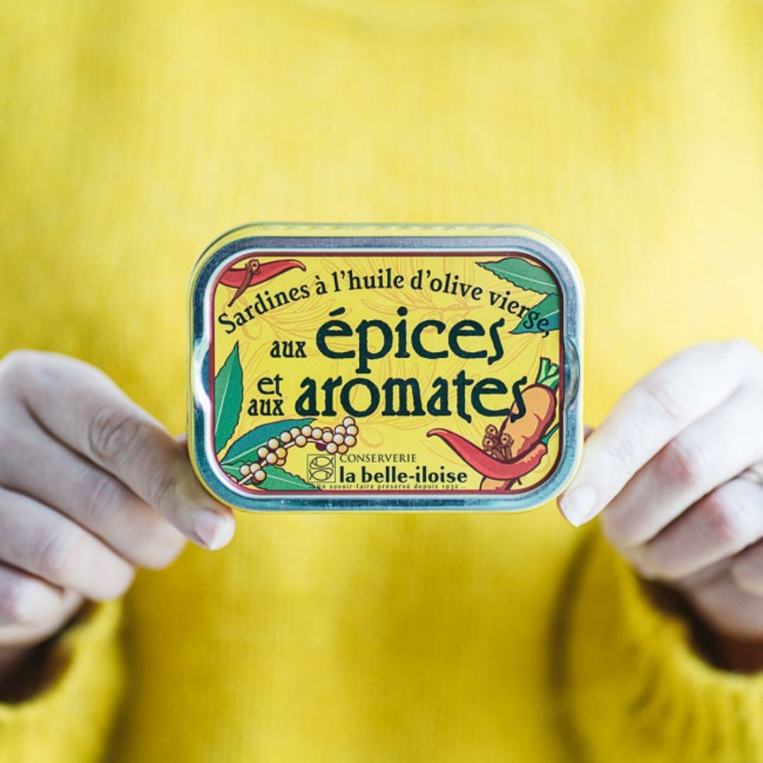 Spiced sardine tin held in two hands, showing its compact palm-sized rectangular shape