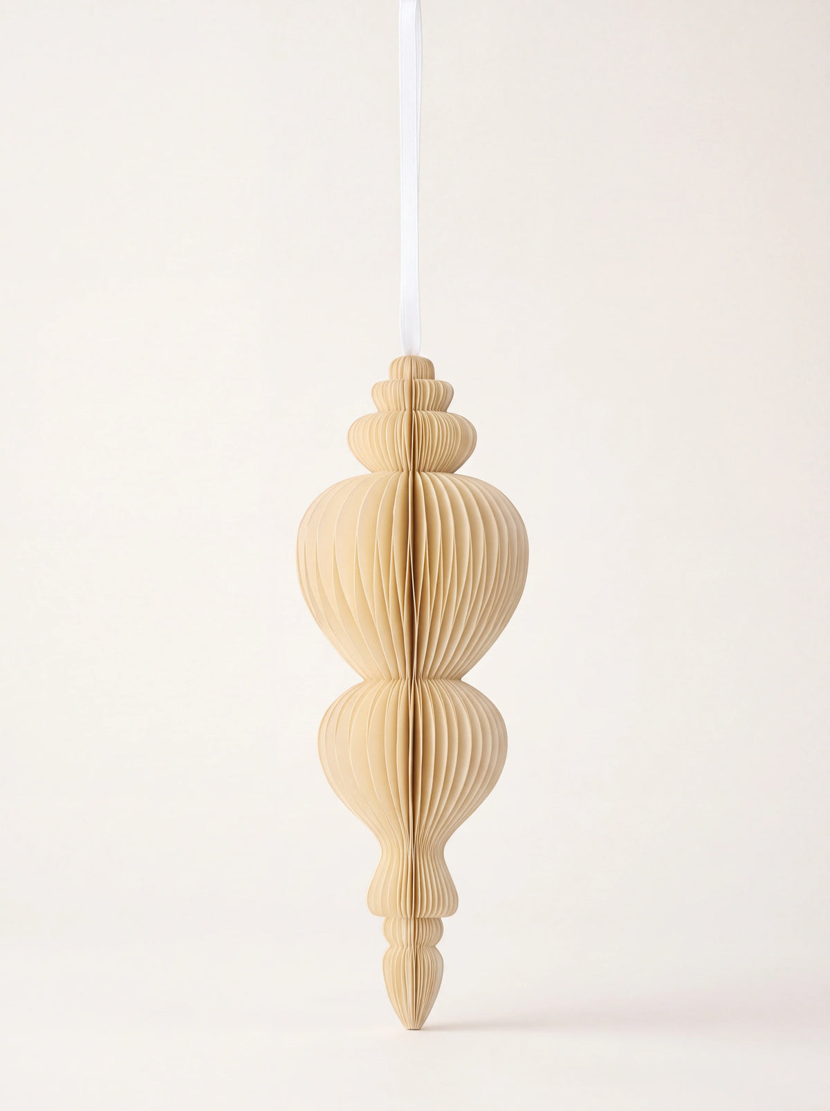 Spire-shaped paper honeycomb ornament in cream with a white hanging ribbon