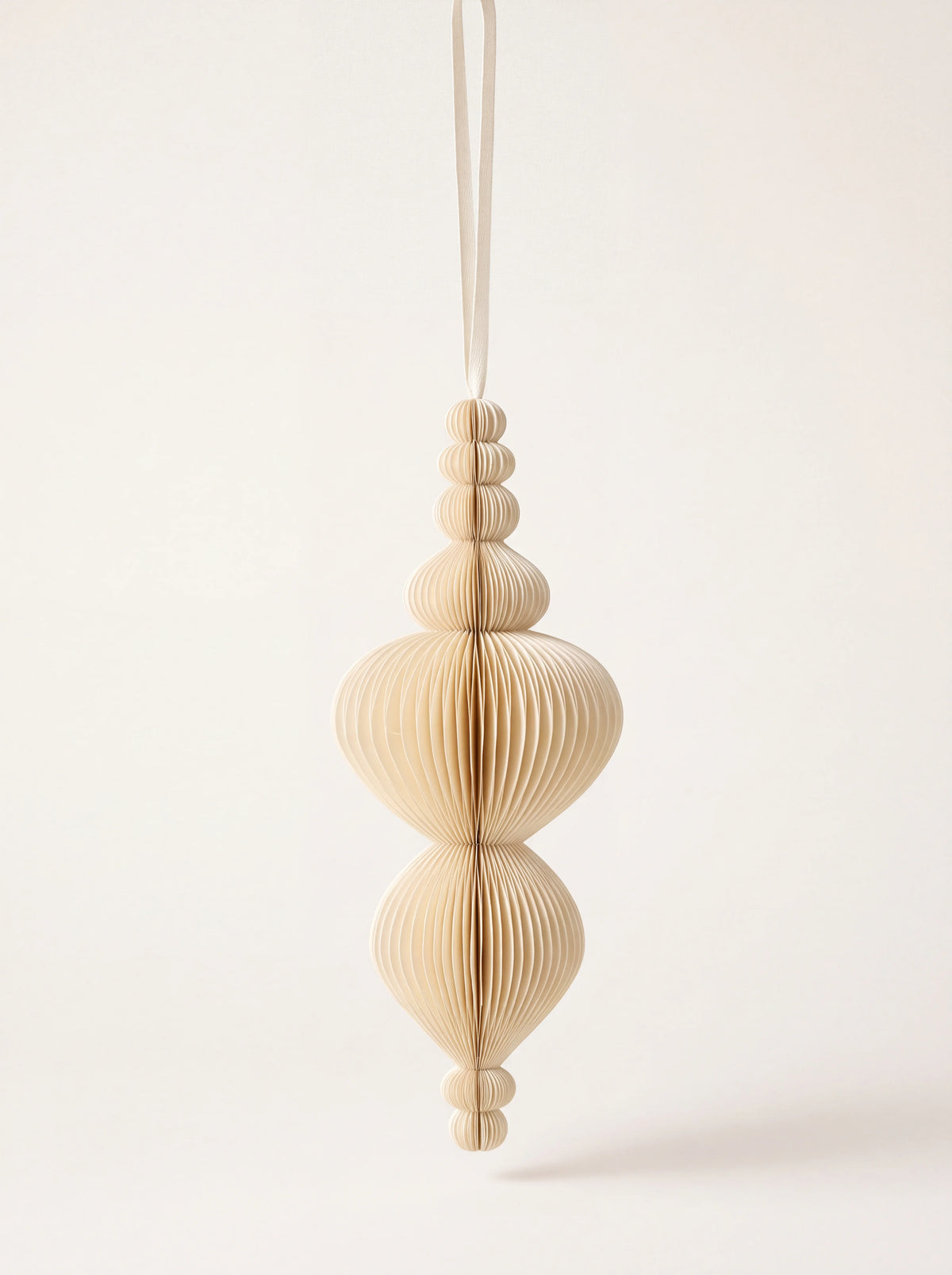 Paper honeycomb ornament in shell tone, with an elongated spire silhouette and hanging ribbon