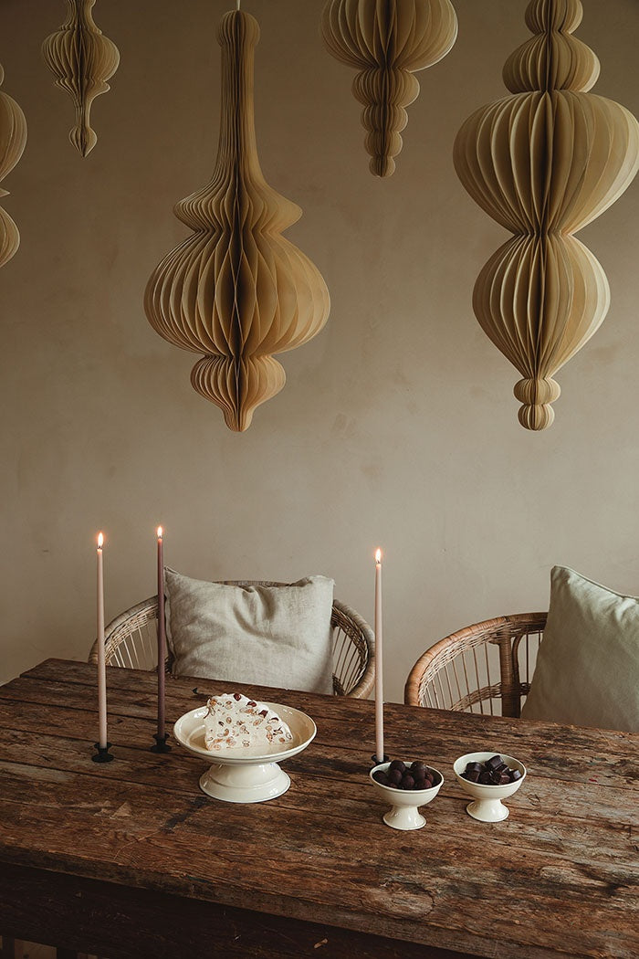 Paper honeycomb spire ornament hanging above a rustic dining table alongside other paper decorations