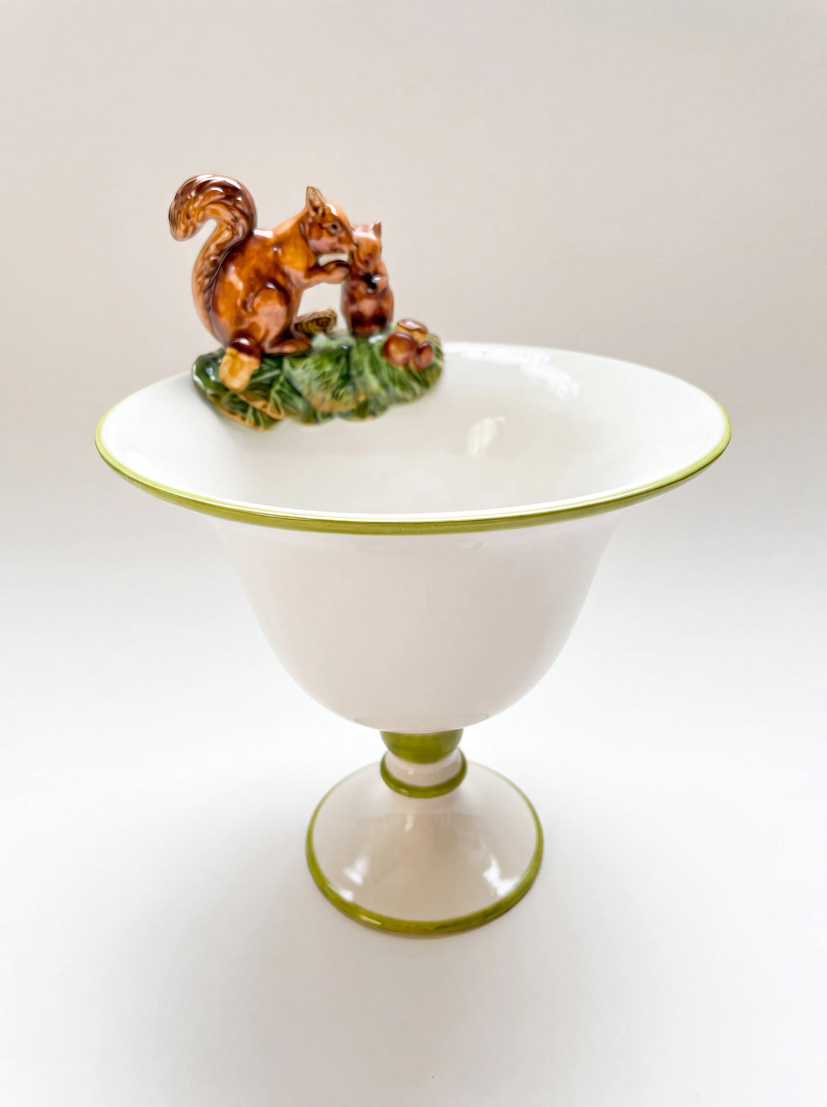 Ceramic pedestal vase in white with green trim and a hand-painted squirrel figurine perched on the rim
