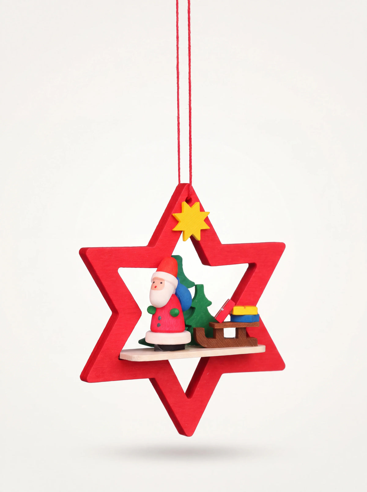 Red wooden star ornament framing a miniature Santa Claus figure, fir tree, sledge and yellow star