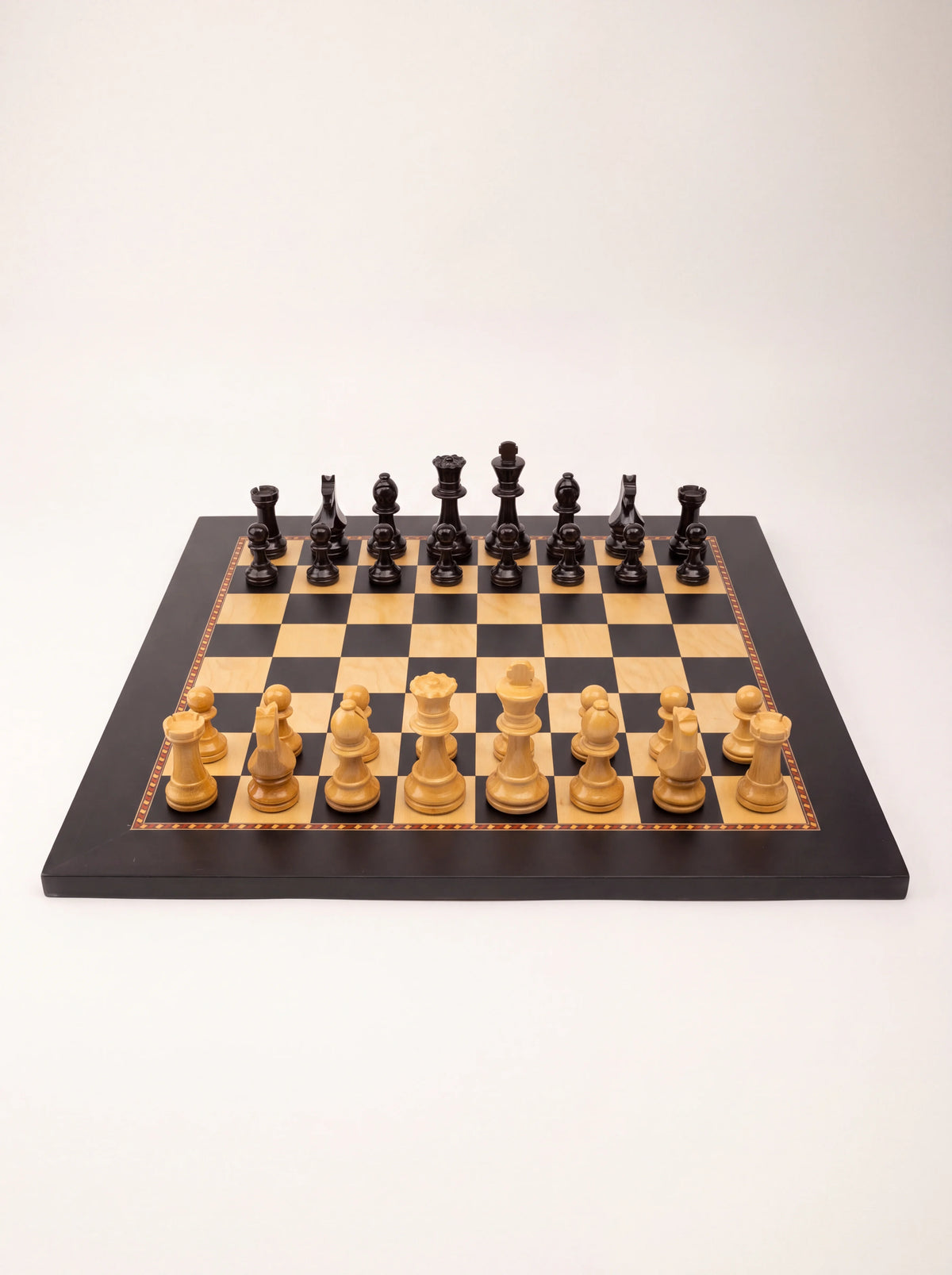 Staunton wooden chess set with light and dark pieces set up on a chequered board with a black border