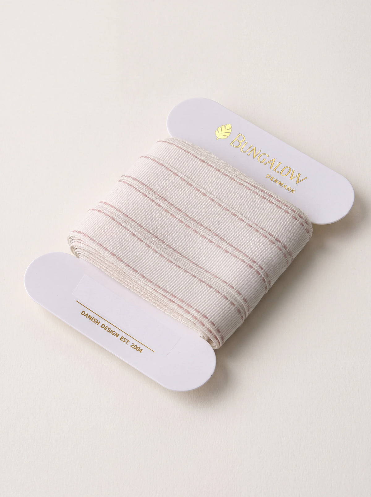 Woven cream ribbon with rose-pink stitched edges, wound on a flat white cardboard spool