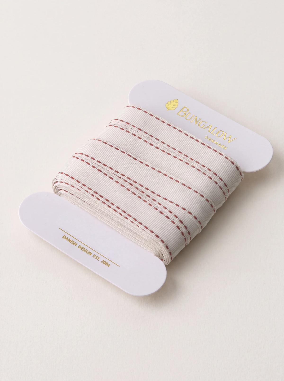 Ribbed cream ribbon with scarlet stitched edges wound on a card labelled Bungalow Denmark