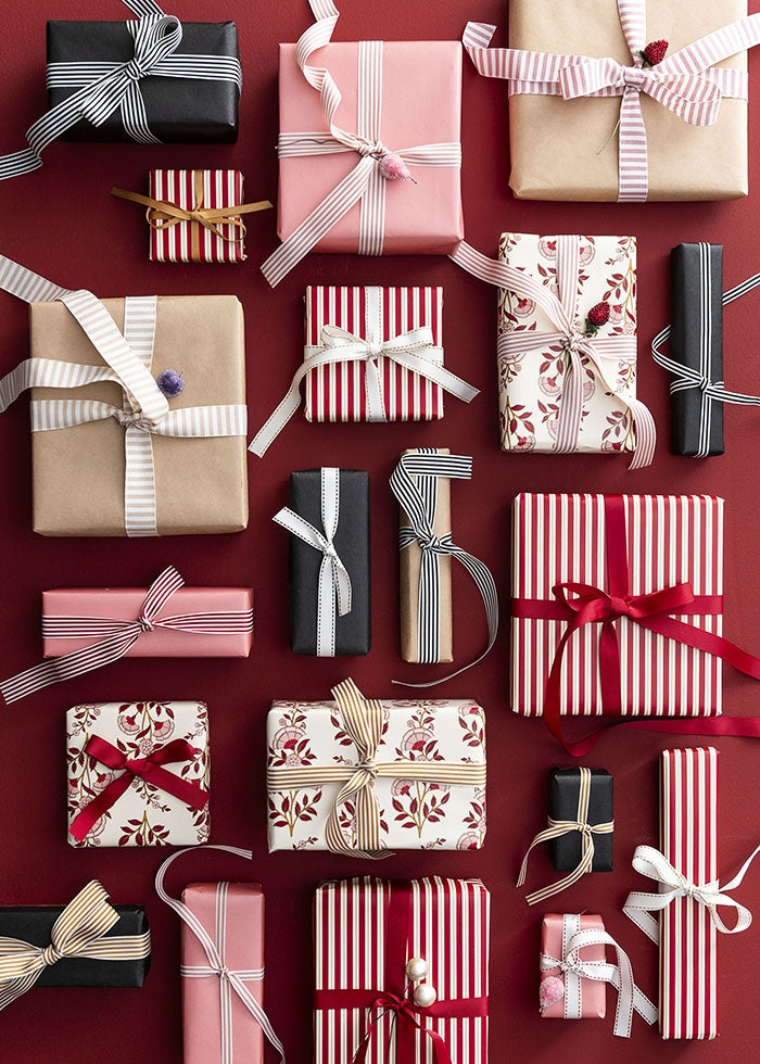 Stitched-edge ribbon tied around wrapped gift boxes amongst assorted presents on a dark red background