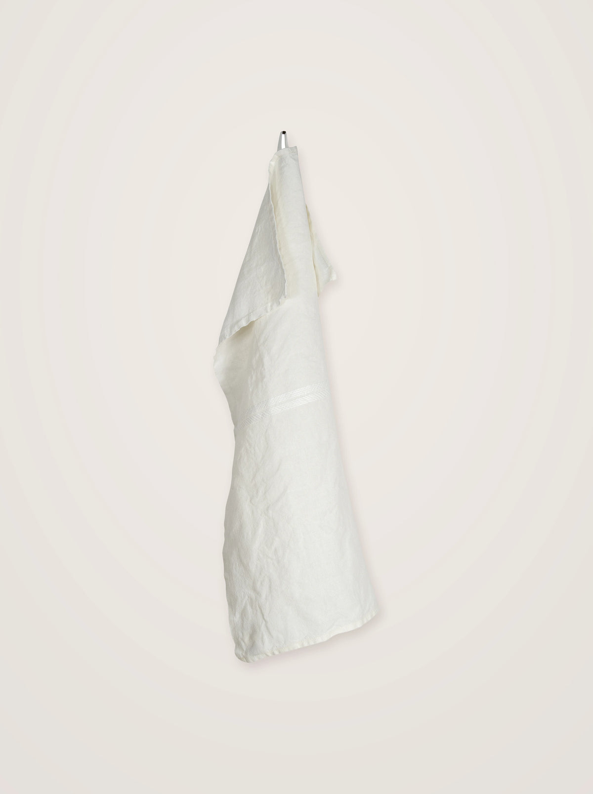 Washed white linen towel suspended by its hanging loop, displaying subtle crinkles and a woven stripe