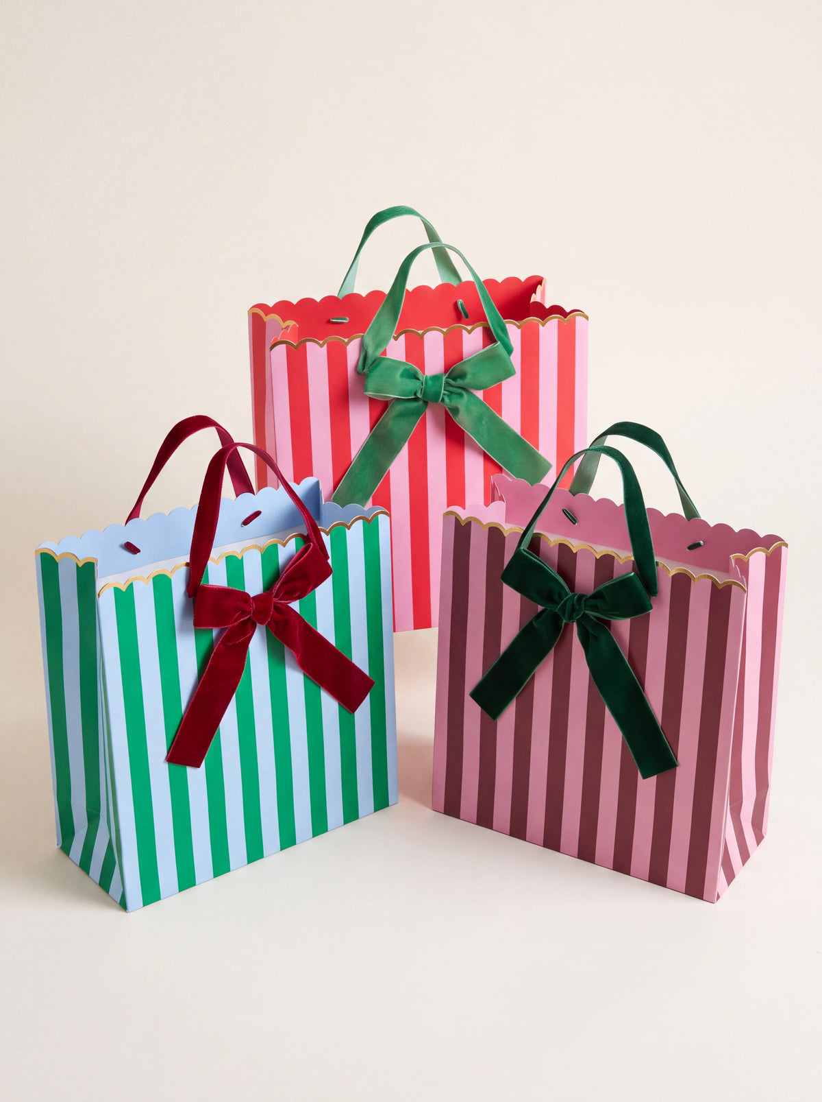 Set of three striped paper gift bags in contrasting colours with scalloped rims and velvet ribbon bows