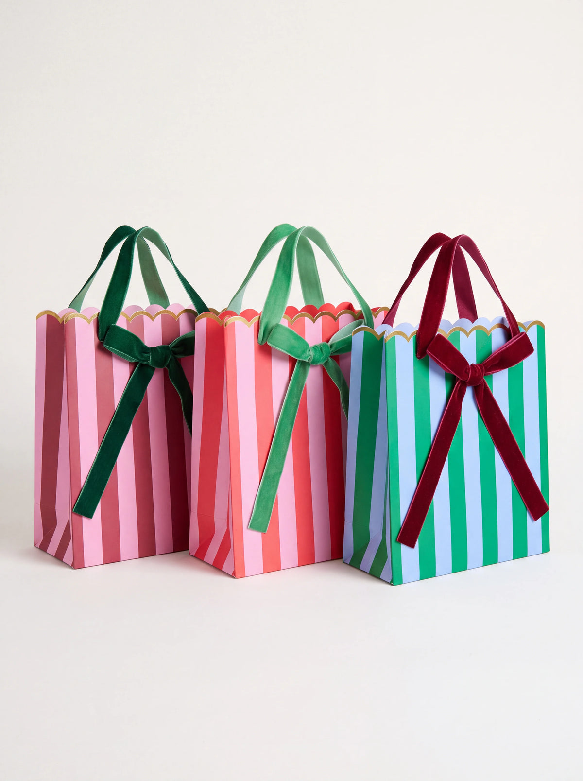 Set of three striped paper gift bags in contrasting colours, with scalloped gold rims and velvet ribbon bows