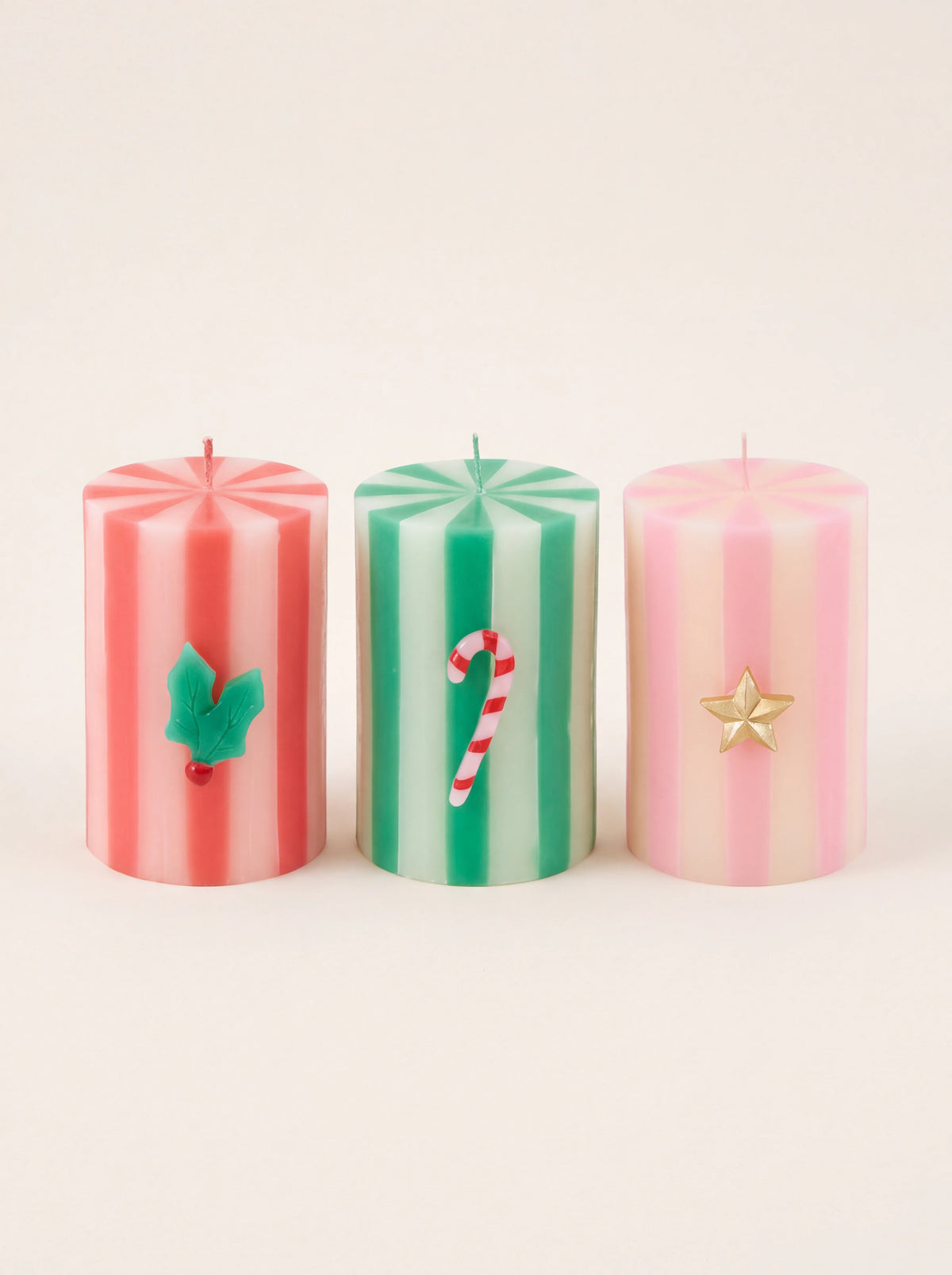 Striped wax pillar candles in red, green and pink, featuring wax holly, candy cane and star motifs