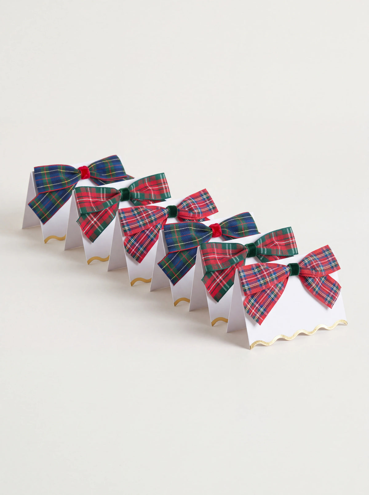 Set of six white paper place cards topped with tartan fabric bows, finished with scalloped gold foil edges