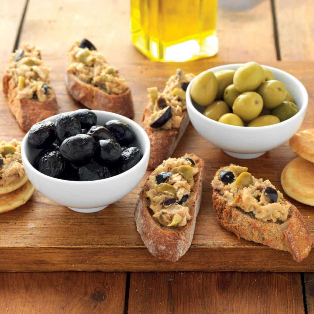 Sardine spread served on crusty baguette slices alongside bowls of black and green olives