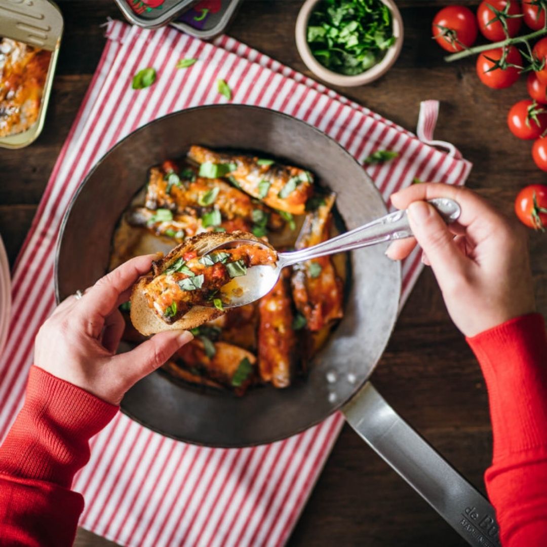 Warm sardines in a skillet, with a portion spooned onto a slice of toasted bread