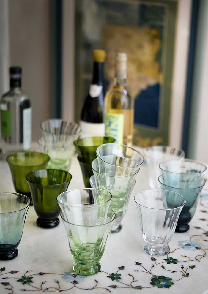 Flared glass tumblers in assorted colours stacked and arranged on a table with wine bottles