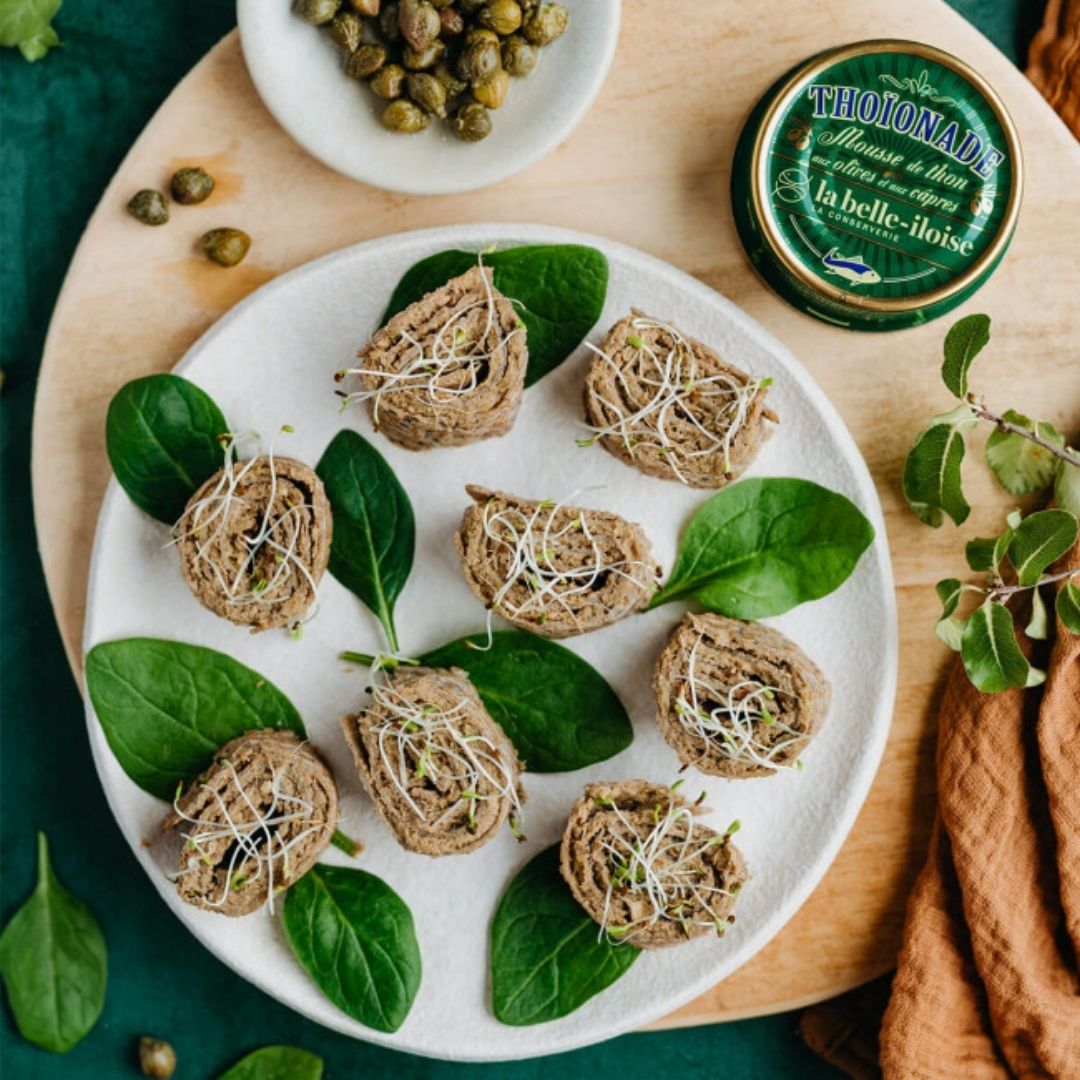 Tuna mousse rolled in savoury crêpe bites garnished with sprouts, served on a plate with spinach leaves