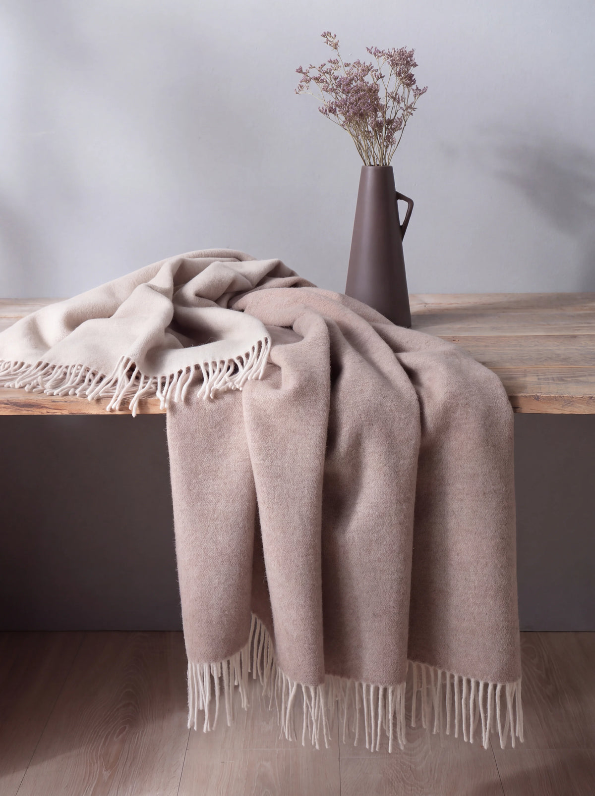 Wool and cashmere blanket draped loosely over a wooden table, showing its soft texture and fringed hem