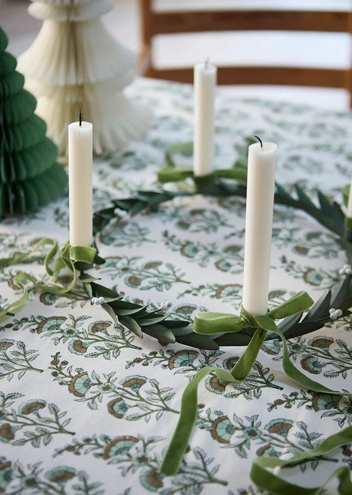 Moss green velvet ribbon tied into bows around white taper candles on a tabletop leaf wreath