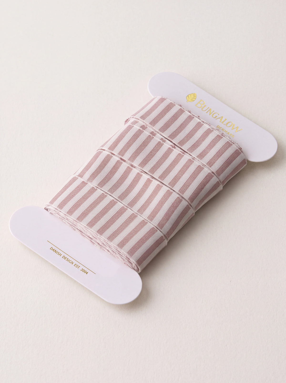 Rose and white vertically striped ribbon wound around a white card spool