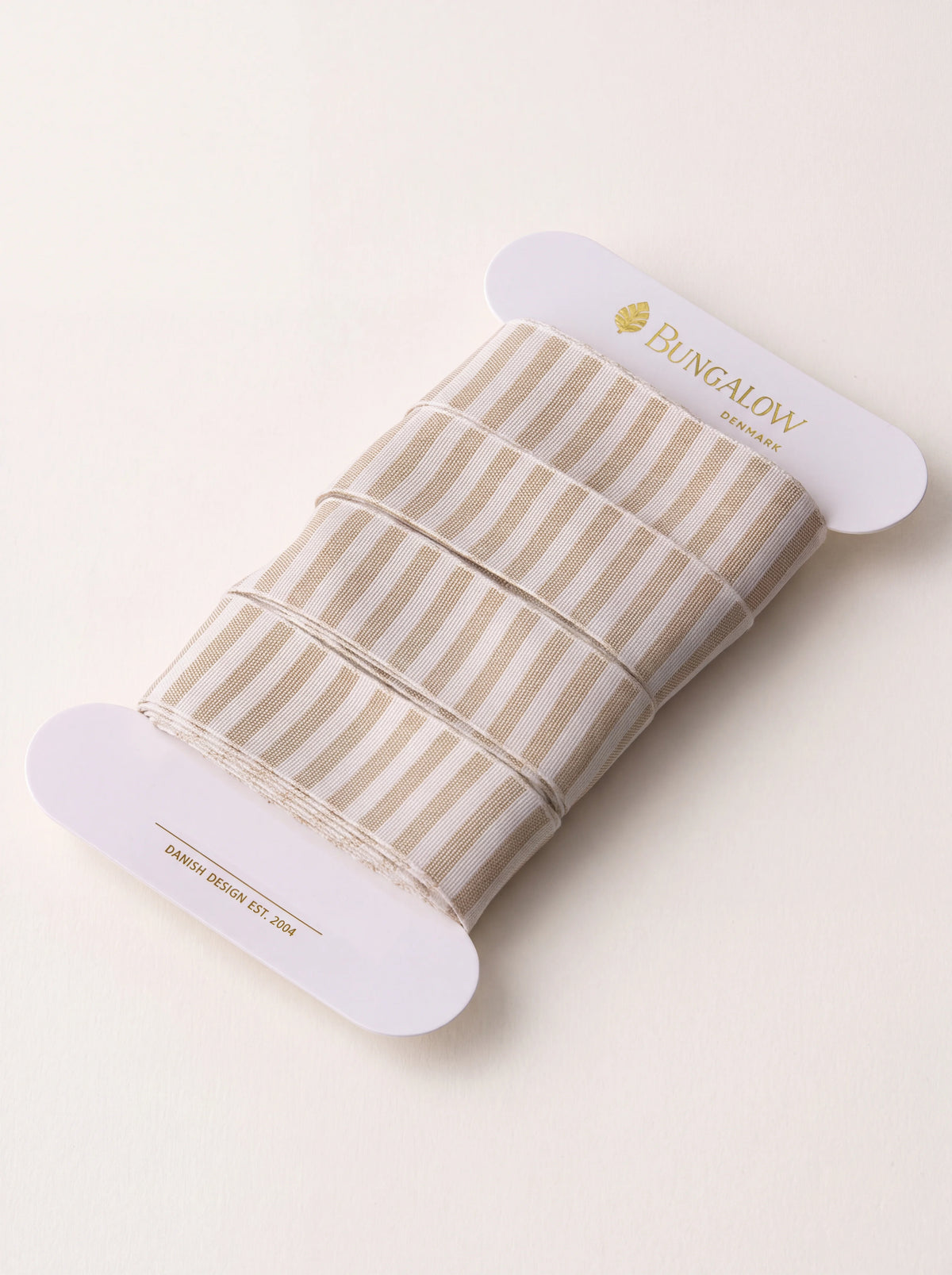 Woven polyester ribbon with sand and white vertical stripes, wound on a flat white card