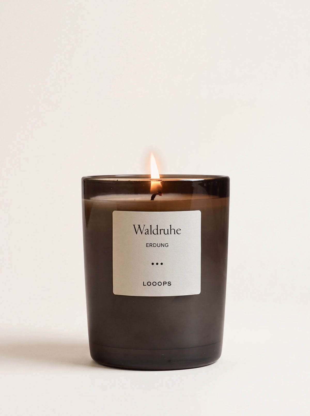 Lit scented candle in a dark glass jar with a label reading Waldruhe ERDUNG LOOOPS