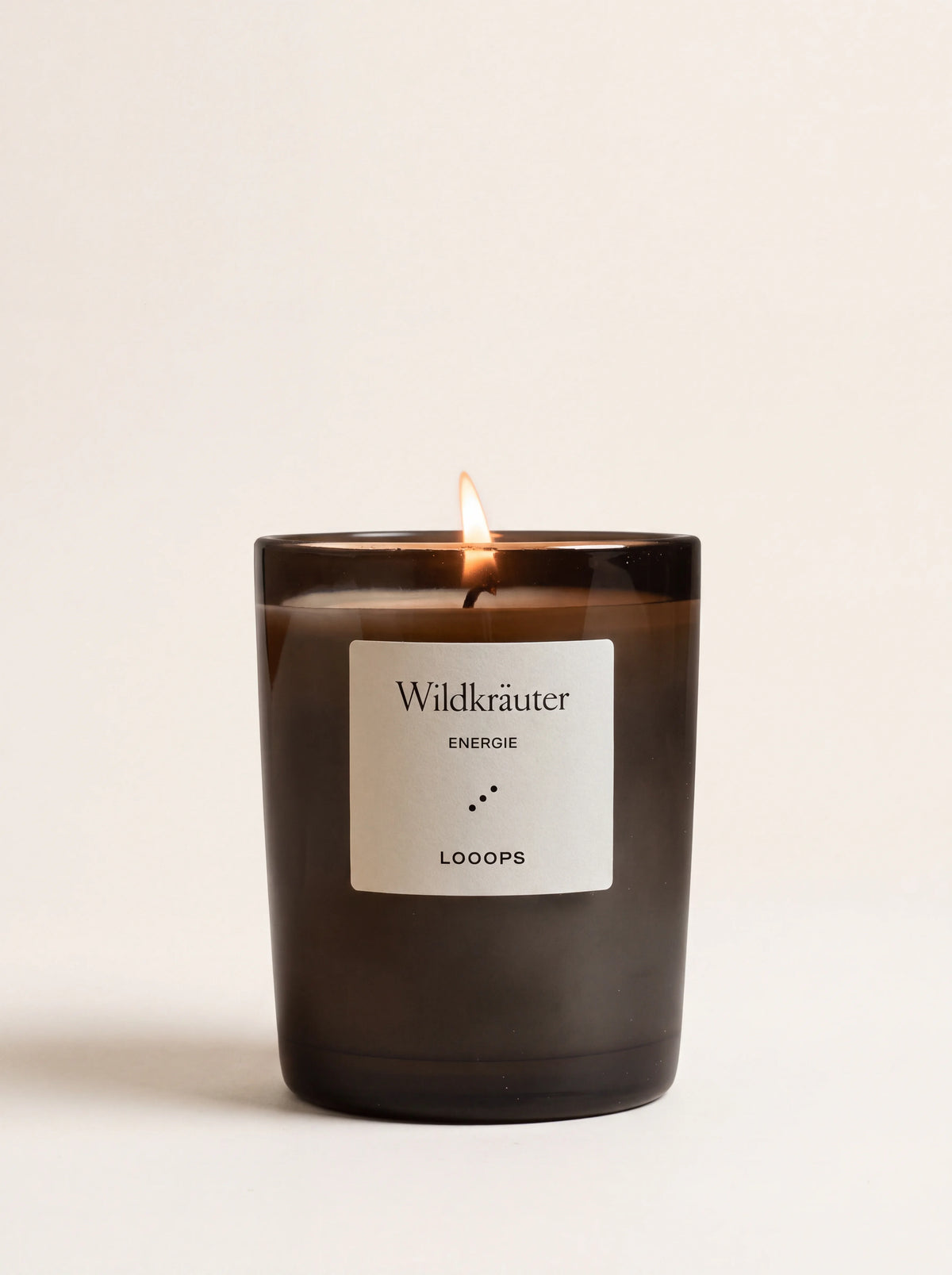 Lit scented candle in a dark glass jar with a label reading Wildkräuter ENERGIE LOOOPS