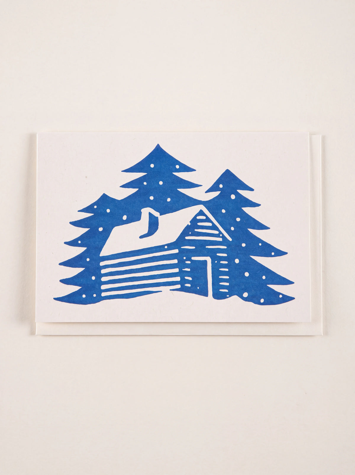 Winter cabin card with a blue letterpress illustration of a snow-covered log cabin among pine trees
