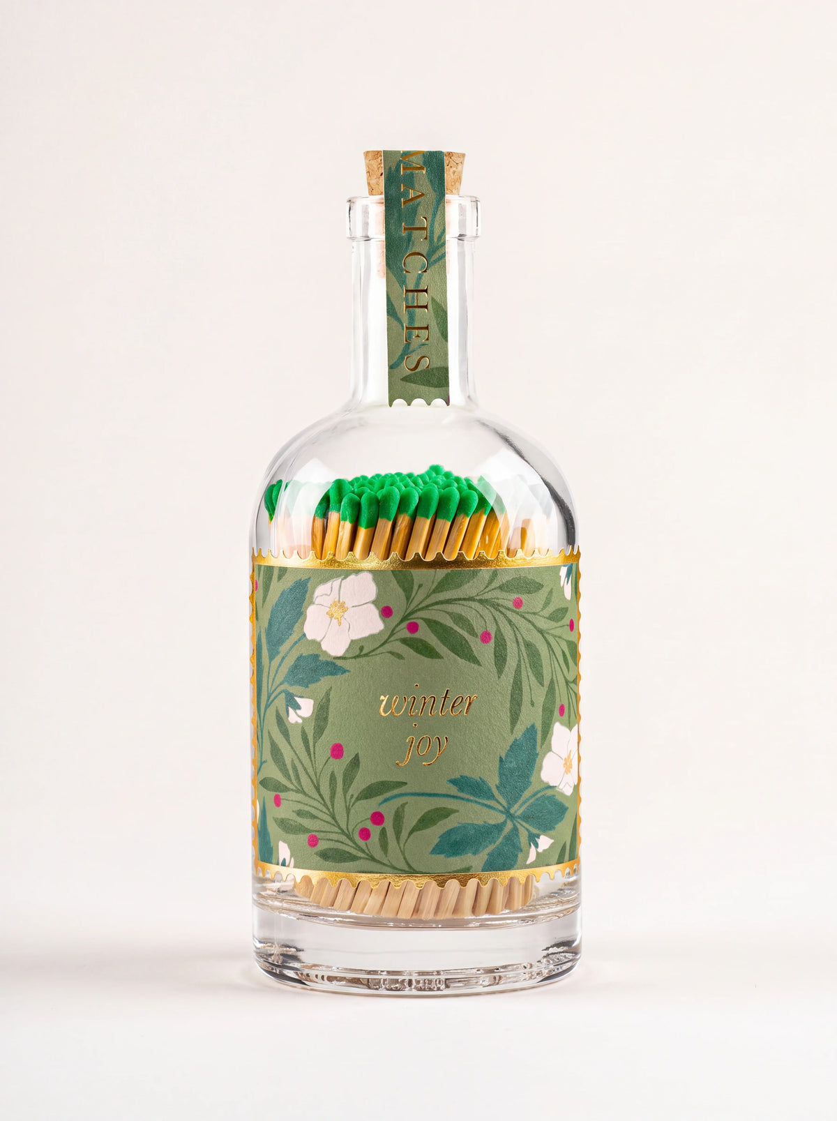 Clear glass match bottle filled with green matches, cork stopper, and floral label reading winter joy