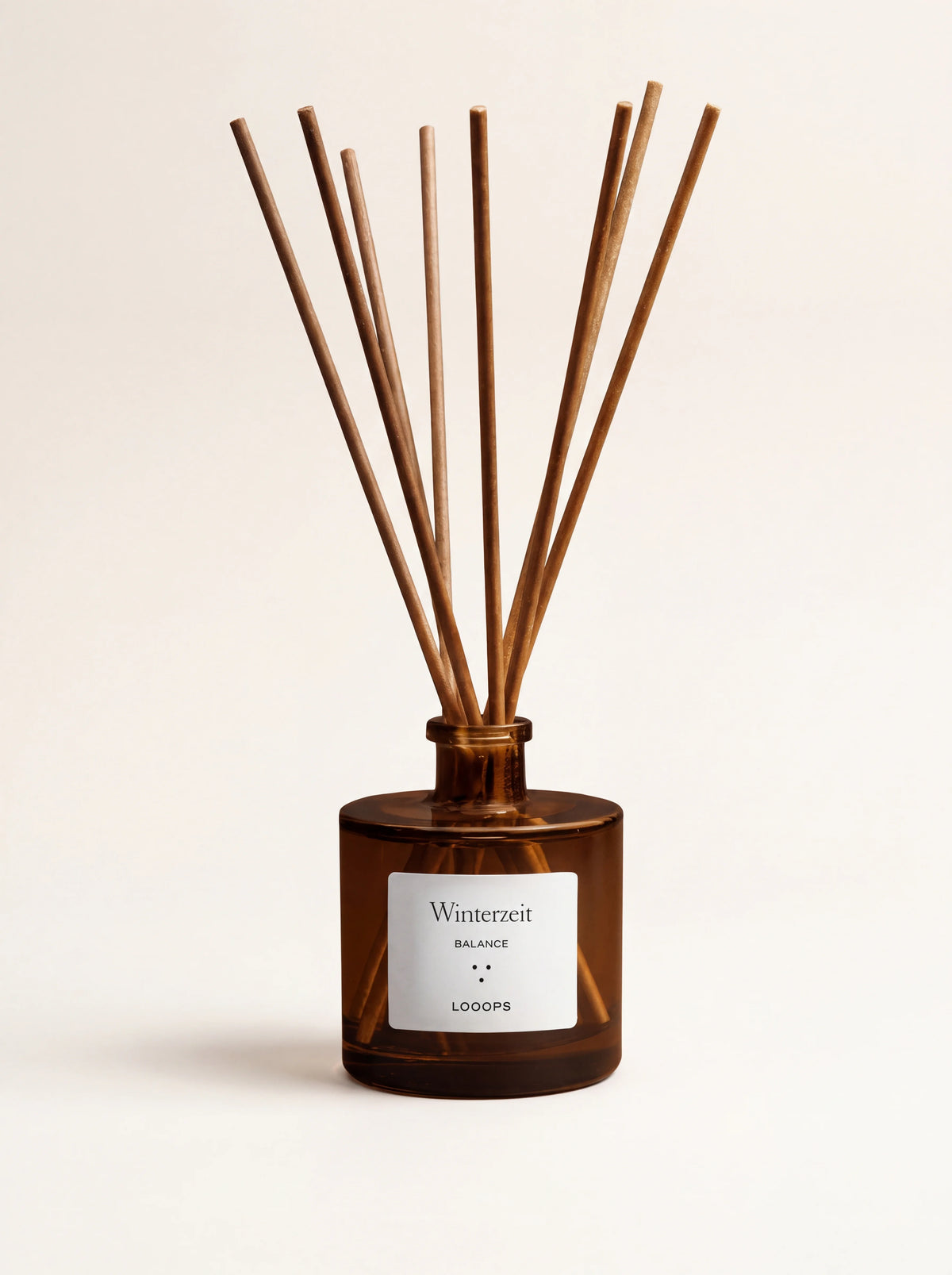 Amber glass reed diffuser with rattan sticks and a label reading Winterzeit BALANCE LOOOPS